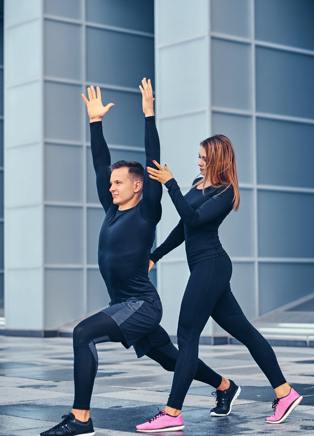 The athletic fitness couple is stretching over modern building background. Full body image.
