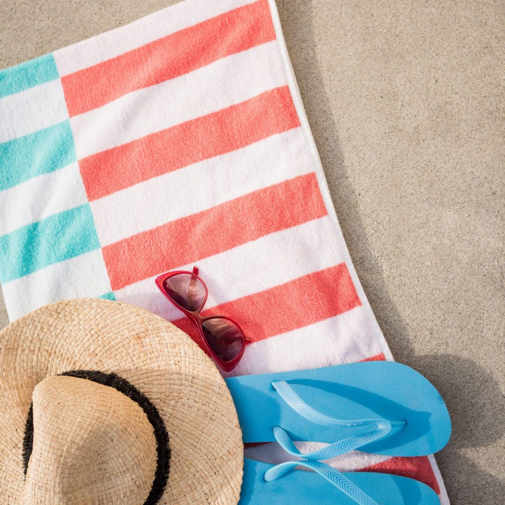 Straw hat, blue flip flop and sunglasses kept on beach blanket at beach